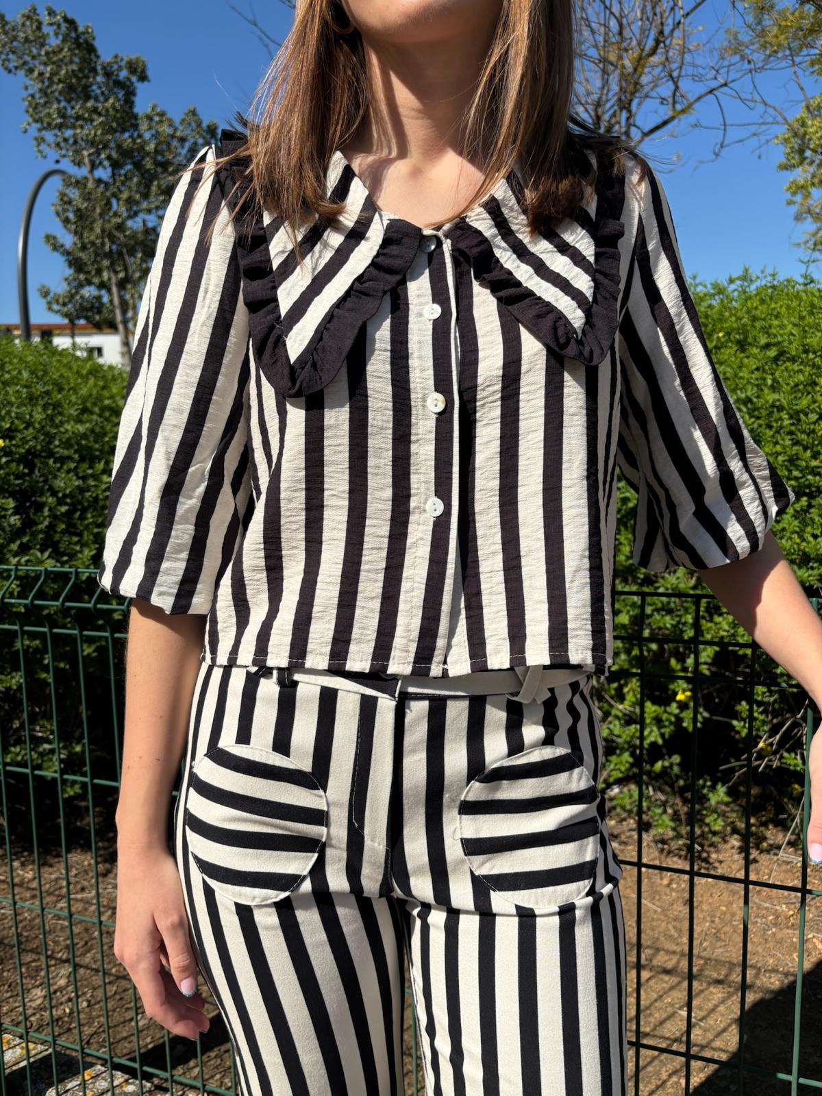 Blusa corta de mujer a rayas con cuello maxi en pico ribeteado con un volante pequeño y manga al codo abullonada. Diseño ligero con botones ideal para looks elegantes y casuales.