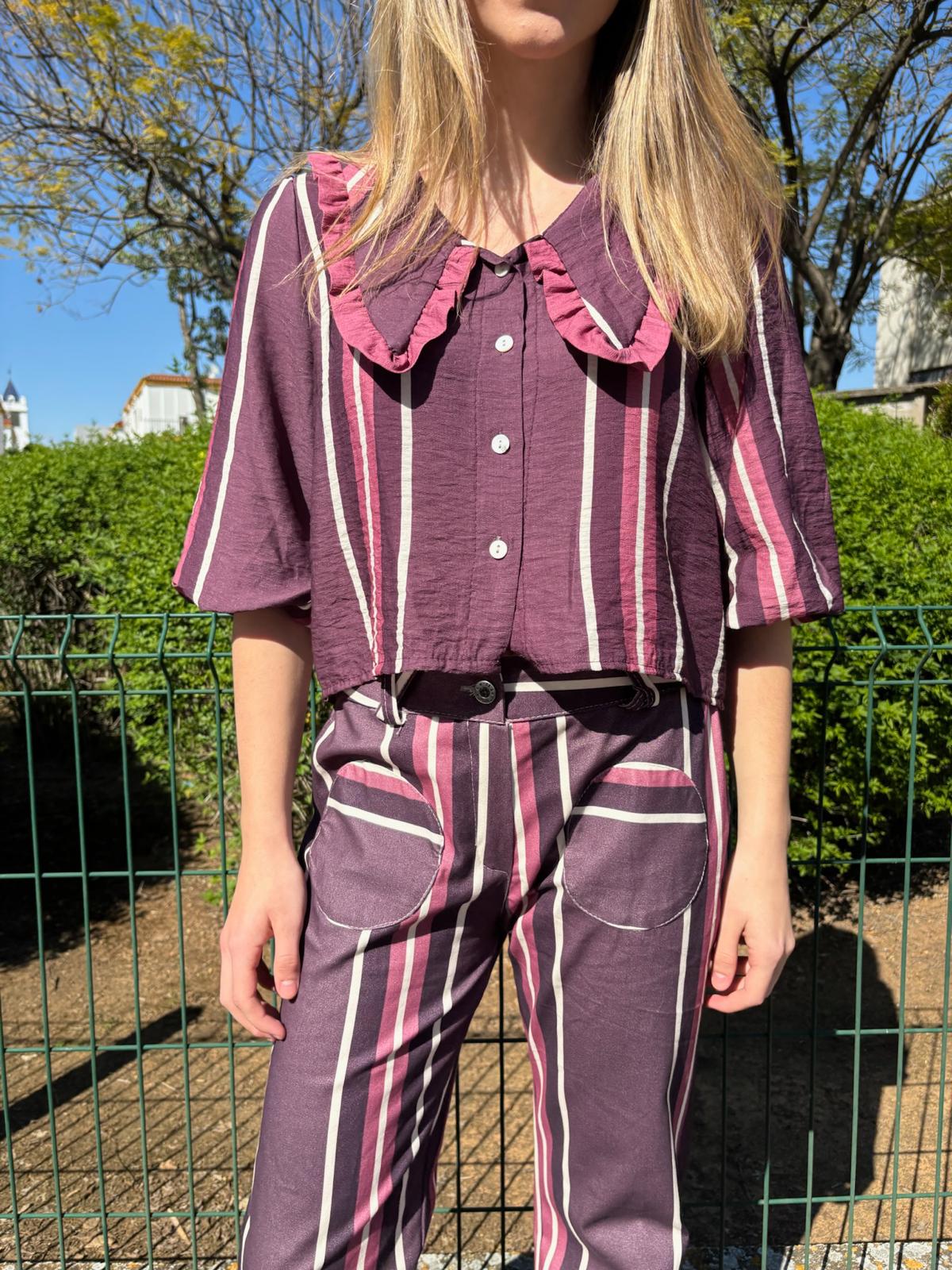 Blusa corta de mujer a rayas con cuello maxi en pico ribeteado con un volante pequeño y manga al codo abullonada. Diseño ligero con botones ideal para looks elegantes y casuales.