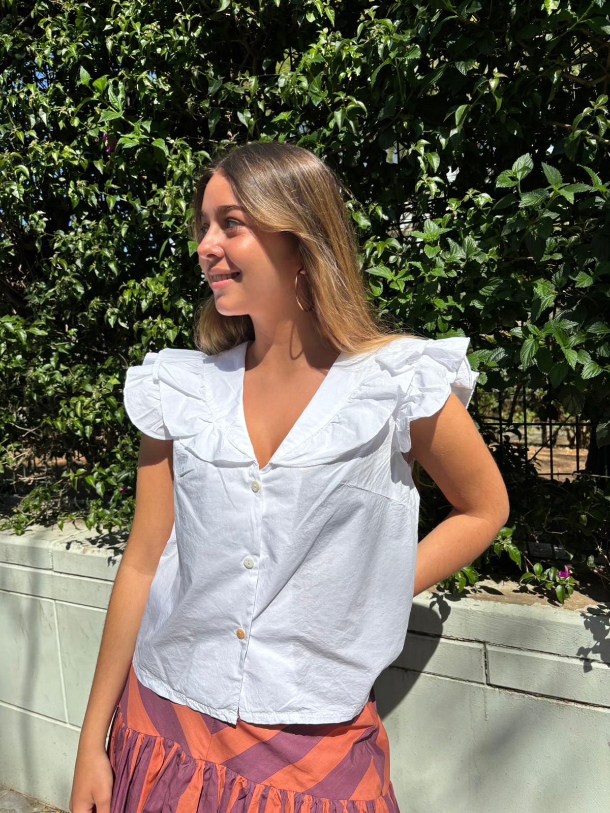Blusa con cuello amplio de volantes y corte fluido. Diseño ligero y femenino, con botones frontales y manga sisa que aporta frescura y estilo elegante.