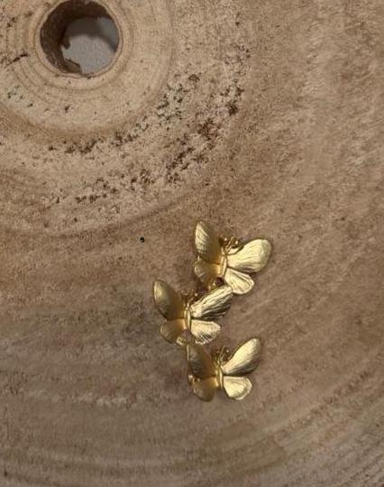 Broche dorado de tres mariposa pequeñas unidas una encima de otra.