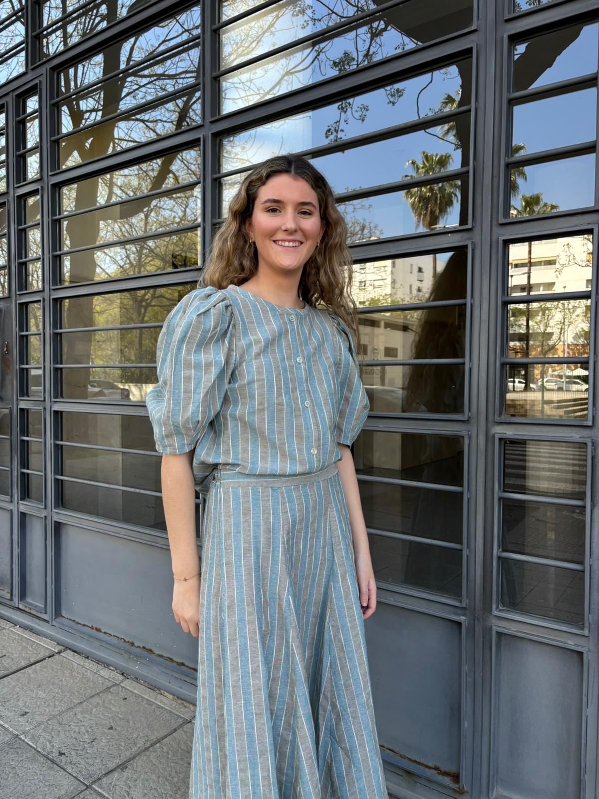 Blusa y falda de rayas verticales en tono azul grisáceo, con manga corta abullonada y botones frontales. Ligera, fresca con ese aire chic que no necesita presentación.